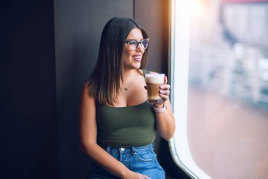 Tatilde mutlu ve kendinden emin gülümseyen genç ve güzel bir kadın. Güvertede durmuş, gülümsüyor, kahve içiyorduk.