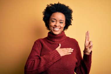 Kıvırcık saçlı, balıkçı yaka kazaklı, gülümseyen, elleri göğsünde ve parmakları havada, sadakat yemini eden güzel Afro-Amerikan kadın.