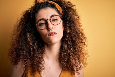 Güzel esmer kadın tatilde, kıvırcık saçlı, piercing takan, gözlüklü ve yüzünde ciddi bir ifade olan. Basit ve doğal bir şekilde kameraya bakıyorsun..