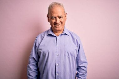 Yüzünde mutlu ve havalı bir gülümseme ile pembe arka planda dikilen, gündelik gömlekler giyen orta yaşlı, beyaz bir adam. Şanslı kişi..