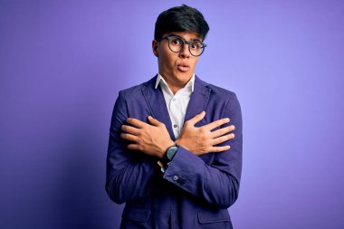 Ceket ve gözlük takan yakışıklı genç bir iş adamı. Mor arka planda. Soğuk kış soğuğu için titriyor ve donuyor.