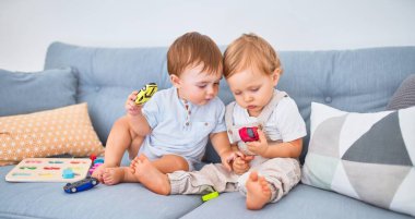 Kanepede oturup evde oyuncaklarla oynayan güzel bebekler.