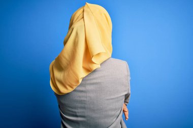 Orta yaşlı esmer iş kadını, geleneksel Müslüman tesettüre bürünmüş mavi arka planda, mutlu ve pozitif bir şekilde sarılıyor. Sevgi ve özgüven.