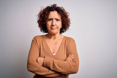 Orta yaşlı güzel kıvırcık saçlı kadın izole edilmiş beyaz arka plan üzerine sıradan bir kazak giyiyor şüpheci ve gergin, yüzünde çapraz kollu tasvip etmeyen bir ifade. Negatif kişi.