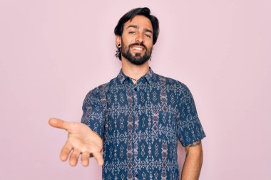 Genç, yakışıklı, bohem, pembe arka planda hippi tarzı giyinmiş neşeli gülümsemeli, yardım eli uzatan ve kabul gören bir adam..