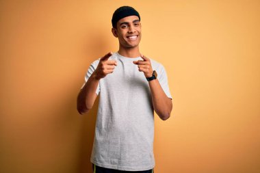 Sarı arka plan üzerine spor giysili yakışıklı Afro-Amerikan sporcusu mutlu ve komik yüzlü parmaklarını kameraya doğrultuyor. İyi enerji ve titreşimler.