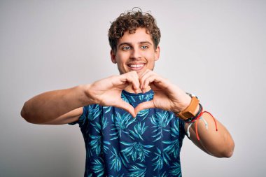 Sarışın, yakışıklı, tatilde, kıvırcık saçlı, sıradan bir yaz tişörtü giymiş, gülümseyen, elleriyle kalp sembolü yapan genç bir adam. Romantik konsept.