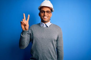 Siyah saçlı, güvenlik kaskı takan, kameraya gülümseyen ve zafer işareti yapan yakışıklı Afro-Amerikan mühendis. İki numara..