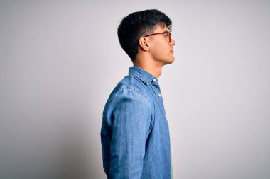 Gözlüklü, rahat gömlekli, gözlüklü genç bir adam beyaz arka plana bakıyor, rahat profil pozu veriyor, kendine güvenen bir gülümsemesi var..