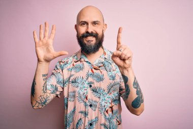 Sakallı ve dövmeli yakışıklı, pembe arka planda sıradan bir çiçek gömleği giyen ve altı numaralı parmaklarıyla gülümseyen, kendinden emin ve mutlu bir adam..