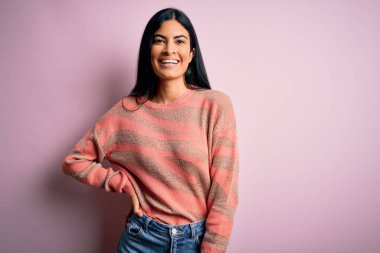Moda kıyafetleri giyen genç ve güzel bir kadın. Manken, sokak tarzı giyiniyor. Pembe arka planda dikiliyor.