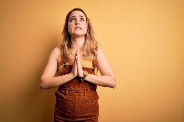 Tulum ve diyabet giymiş genç güzel sarışın kadın sarı arka planda duruyor. Elleri bağlı yalvarıyor ve dua ediyor. Yüzünde umut ifadesi var. Yalvarıyorum..