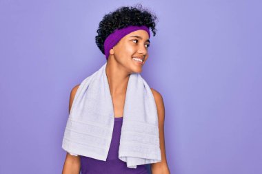 Güzel Afro-Amerikan sportif kadın spor yapıyor mor arka plan üzerine havlu giyip yüzünde gülümsemeyle, doğal ifadeyle yan yana bakıyor. Kendinden emin gülen.