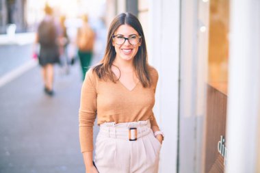 Mutlu ve kendinden emin gülümseyen genç ve güzel bir kadın. Kasaba caddesinde yüzünde gülümsemeyle dikilirken