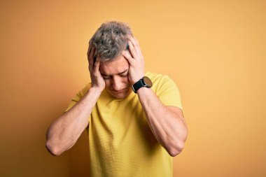 Sarı arka plan üzerine sarı tişört giyen yakışıklı modern bir adam acı ve migrenden dolayı çaresiz ve stresli bir baş ağrısından muzdarip. Ellerini başının üstüne koy..