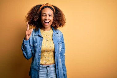 Güzel Afro saçlı Afrikalı Amerikalı sarı izole edilmiş arka planda duruyor ve başarılı bir fikirle işaret ediyor. Heyecanlı ve mutlu. Bir numara..