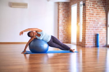 Orta yaşlı güzel sporcu kadın mutlu gülümsüyor. Spor salonunda yoga sınıfında spor topu kullanarak esneme hareketi.