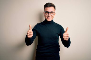 Gözlük takan yakışıklı beyaz bir adam ve izole edilmiş arka plan başarısı tabelasının üzerine süveter giyiyor. Elleriyle olumlu jest yapıyor, gülümsüyor ve mutlu. Neşeli ifade ve kazanan jest.