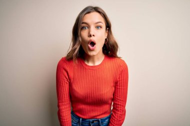İzole edilmiş arka plan üzerinde gündelik kırmızı süveter giyen genç sarışın kız şaşkınlık dolu bir ifade, korku ve heyecan dolu bir yüz ifadesiyle dehşete düşmüş ve şok olmuştu..