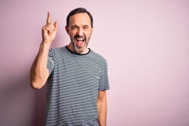 İzole edilmiş pembe arka planda duran sıradan çizgili tişört giyen orta yaşlı, beyaz bir adam başarılı bir fikri işaret ediyor. Heyecanlı ve mutlu. Bir numara..