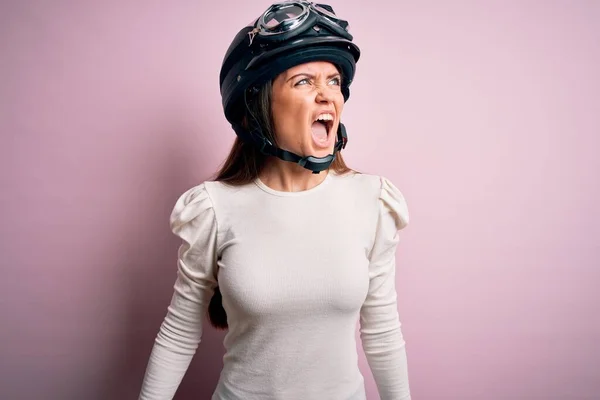 青い目をした若い美しいバイク乗りの女性は 怒りで叫んで ピンクの背景の怒りと怒りの上に元ヘルメットを身に着けています 激怒と積極的な概念 — ストック写真