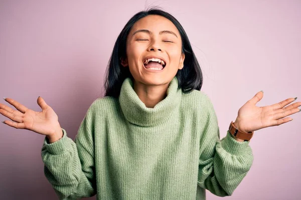 孤立したピンクの背景にタートルネックセーターを身に着けている若い美しい中国の女性は 腕を上げ 興奮叫んで目を閉じて成功のために狂気と狂気を祝う 勝者のコンセプト — ストック写真