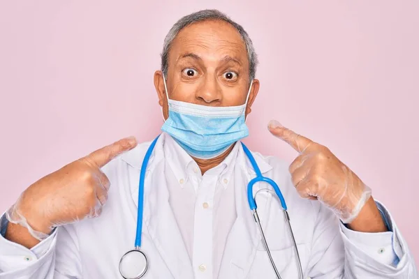 シニアHoary医師男身に着けています医療マスクと聴診器上のピンクの背景非常に幸せなポインティングとともに手と指 — ストック写真