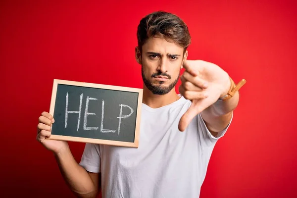 Young man with problem holding blackboard with help message over red bakground with angry face, negative sign showing dislike with thumbs down, rejection concept