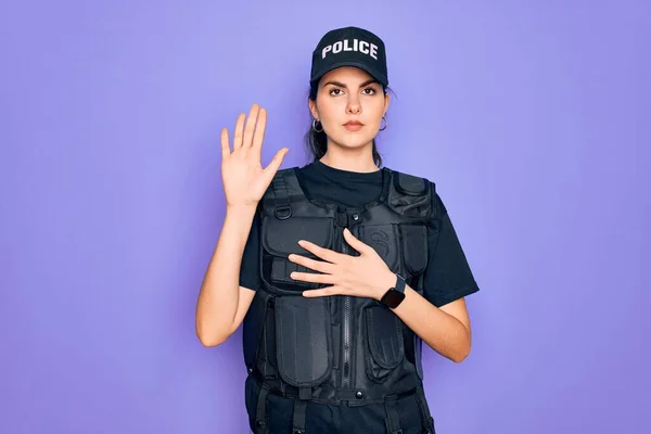 Young police woman wearing security bulletproof vest uniform over purple background Swearing with hand on chest and open palm, making a loyalty promise oath
