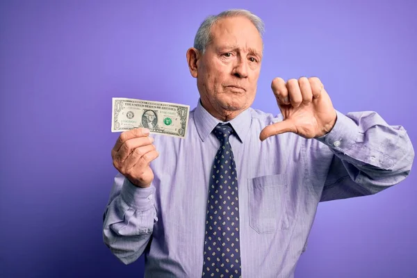 Starszy Siwowłosy Mężczyzna Trzymający Banknot Dolarowy Fioletowym Tle Wściekłą Twarzą — Zdjęcie stockowe