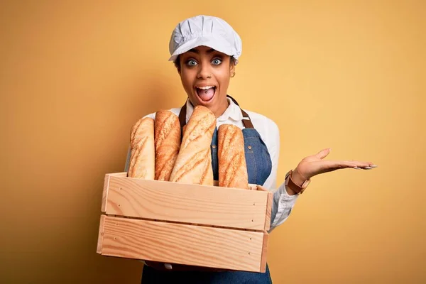 パンと木製の箱を保持エプロンを身に着けている若いアフリカ系アメリカ人のパン屋の女の子は非常に幸せと興奮 大きな笑顔で叫んで勝利を祝う勝者式と手を上げ — ストック写真