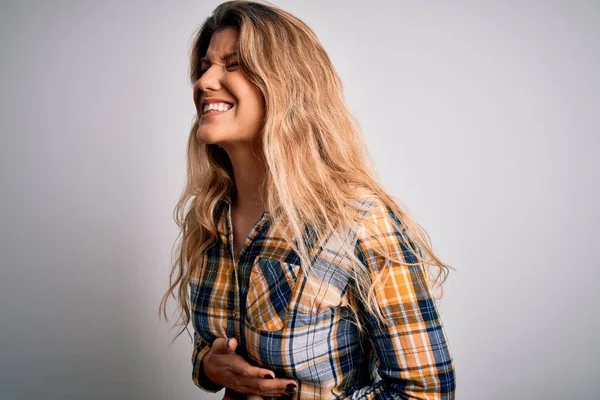 Young beautiful blonde woman wearing casual shirt standing over isolated white background with hand on stomach because nausea, painful disease feeling unwell. Ache concept.