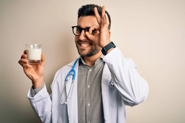 若いです医師男身に着けていますStethoscope保持Aガラスのミルク上に隔離された背景とともに幸せな顔笑顔行いますOk Signとともに手で目を通して指 — ストック写真