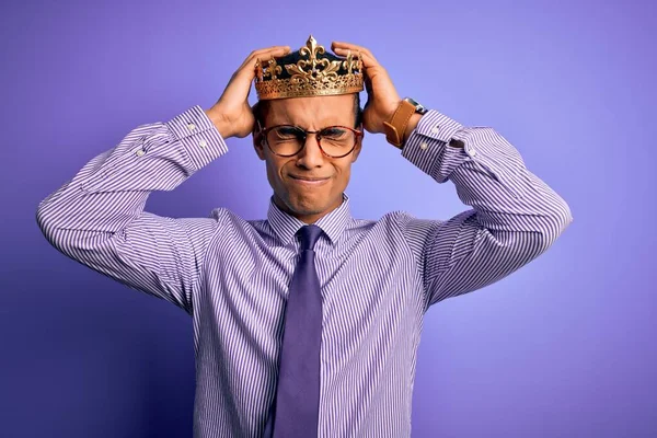 痛みや片頭痛のため 絶望的な頭痛やストレスに苦しんで紫色の背景に王の黄金の冠を身に着けている若いハンサムなアフリカ系アメリカ人男性 手を頭に — ストック写真