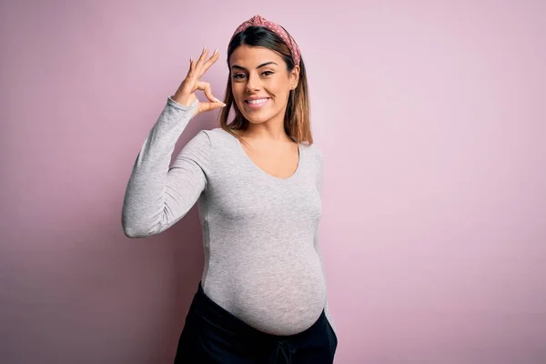 若い美しいブルネットの女性は 孤立したピンクの背景の上に赤ちゃんを期待し 手と指でOkサインをして肯定的な笑顔 成功した表現 — ストック写真