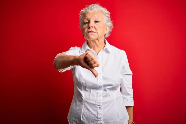 年长的漂亮女人穿着雅致的衬衫站在孤立的红色背景之上 看起来不高兴 表现出拒绝和负面的大拇指向下的手势 不好的表达方式 — 图库照片