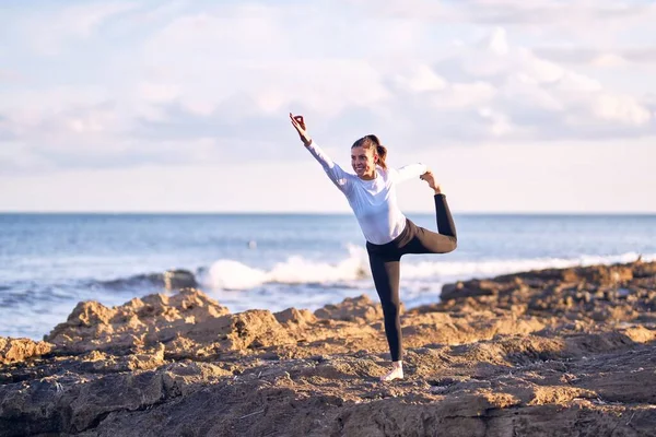 年轻美丽的女运动员笑着快乐地练习瑜伽 教练脸上挂着笑容教武士在海滩上摆姿势 — 图库照片