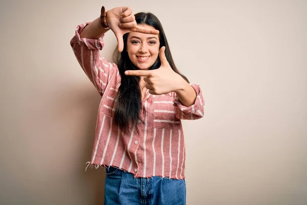 年轻的黑发女人穿着宽松的条纹衬衫 背对孤立的背景 微笑着 用双手和手指做框架 脸上带着快乐的表情 创意和摄影概念 — 图库照片