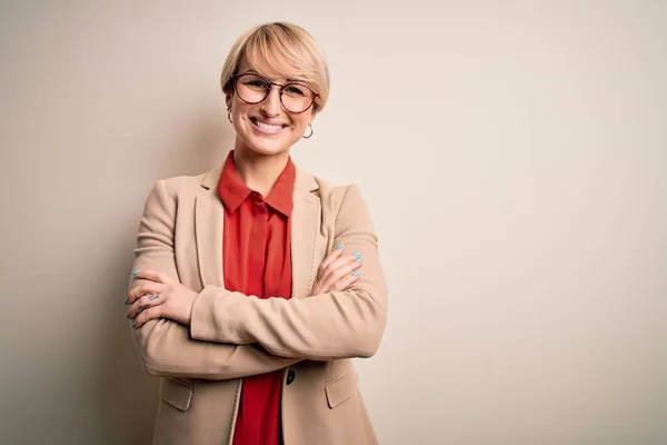 Young blonde business woman with short hair wearing glasses and elegant jacket happy face smiling with crossed arms looking at the camera. Positive person.