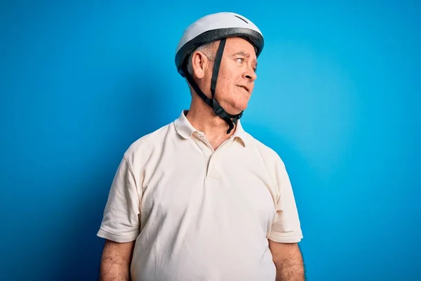 Middle age hoary cyclist man wearing bike security helmet over isolated blue background looking away to side with smile on face, natural expression. Laughing confident.