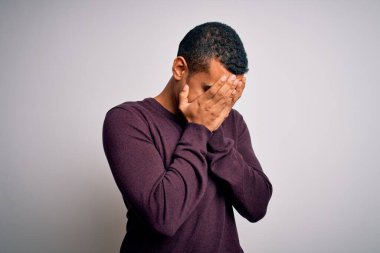 Beyaz arka plan üzerine gündelik süveter giyen genç ve yakışıklı Afro-Amerikan bir adam. Ağlarken suratını ellerle kapatan üzgün bir ifade. Depresyon kavramı.