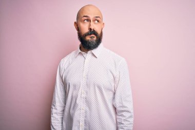 Yakışıklı, kel, sakallı, zarif tişörtlü, soyutlanmış pembe arka planda gülümseyen ve kafasını çeviren bir adam..