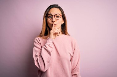 Mavi gözlü, pembe arka planda süveter ve gözlük takan güzel sarışın kadın sessiz olmak istiyor. Sessizlik ve gizli konsept.