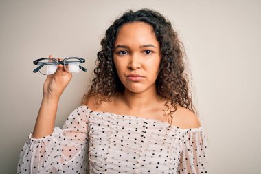 Kıvırcık saçlı, beyaz arka planda görüş gözlüğü takan, zeki yüzlü, kendine güvenen ve ciddi düşünen güzel bir optik kadın.