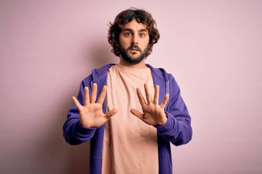 Sakallı, pembe arka planda sıradan bir kazak giyen genç yakışıklı sporcu. Avuçlarını kaldırıyor, reddediyor ve iğrenç bir ifadeyle reddediyor. Dur ve yasakla.