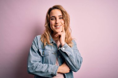 Pembe arka planda sıradan bir kot ceket giyen genç ve güzel sarışın kadın kameraya kollarını kavuşturup gülümseyerek bakıyor ve çenesini kaldırıyor. Olumlu düşünüyorum..