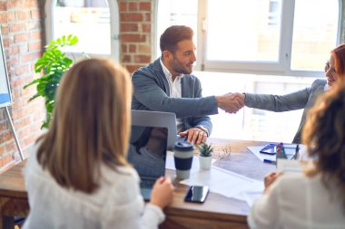 Bir grup iş adamı mutlu ve kendinden emin gülümsüyor. Ofiste anlaşmak için gülümseyerek el sıkışıyoruz.