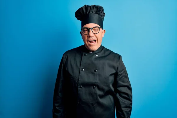 Middle age handsome grey-haired chef man wearing cooker uniform and hat winking looking at the camera with sexy expression, cheerful and happy face.