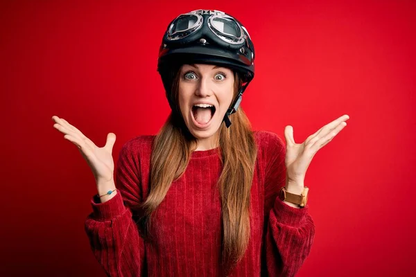 赤い背景の上に元ヘルメットをかぶっている若い美しい赤毛の元サイクリストの女性は 腕を上げて興奮して叫んで目を開けて成功したことに狂気と驚きを祝います 勝者のコンセプト — ストック写真