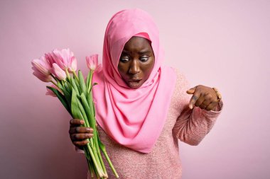 Genç Afro-Amerikan artı cüsseli kadın elinde pembe lale buketi tutuyordu. İlan veren parmaklarıyla işaret ediyordu. Şaşırmış yüz ve ağzı açıktı.